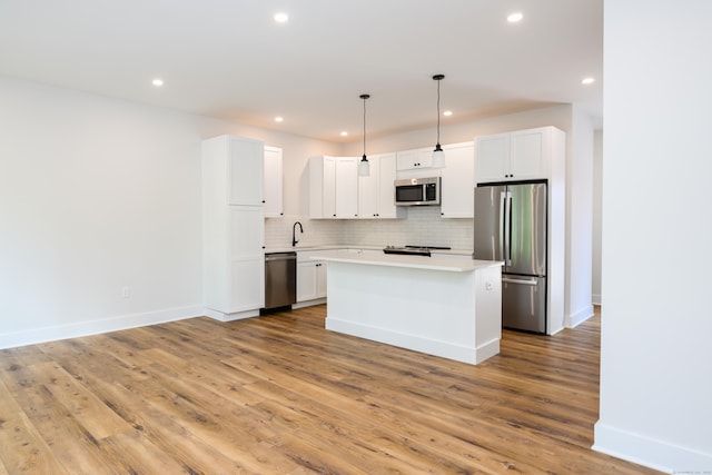 kitchen featuring white cabinetry, light countertops, appliances with stainless steel finishes, hanging light fixtures, and a center island