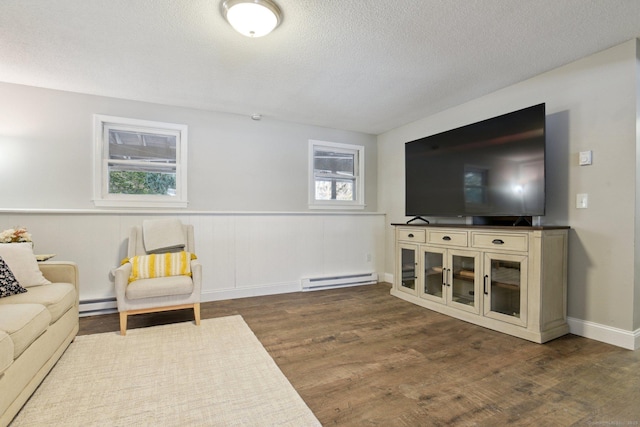 living room with a textured ceiling, baseboard heating, dark wood-type flooring, and wainscoting