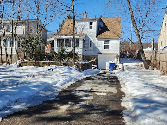 view of front of home featuring a shingled roof, stone siding, a chimney, an attached garage, and fence