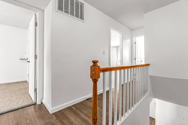 hallway featuring baseboards, visible vents, wood finished floors, and an upstairs landing