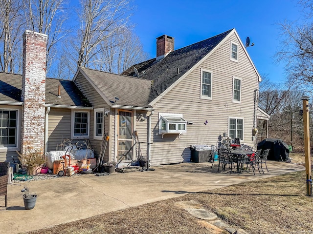 back of house with a patio area, roof with shingles, and a chimney