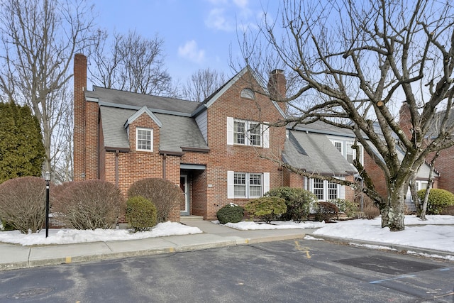 view of front facade with brick siding, a chimney, and a shingled roof