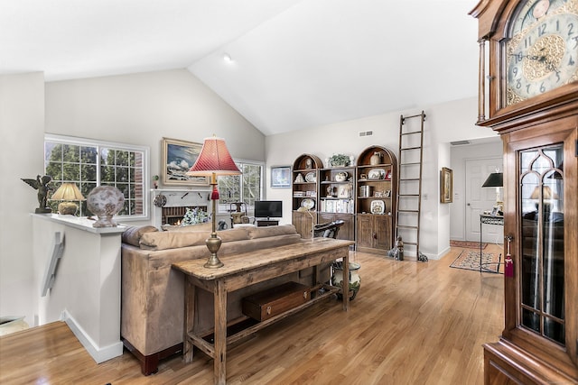 living area featuring a warm lit fireplace, high vaulted ceiling, wood finished floors, and baseboards