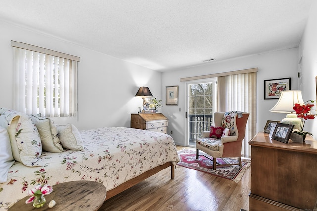 bedroom with a textured ceiling, dark wood-style flooring, visible vents, and access to exterior