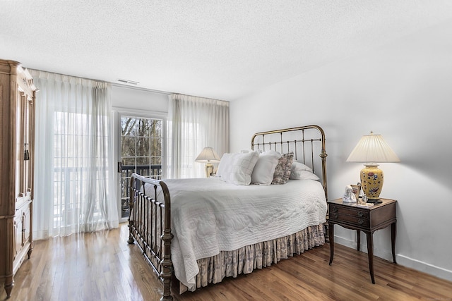 bedroom featuring visible vents, a textured ceiling, baseboards, and wood finished floors