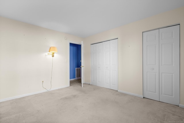 unfurnished bedroom featuring visible vents, baseboards, multiple closets, and light colored carpet