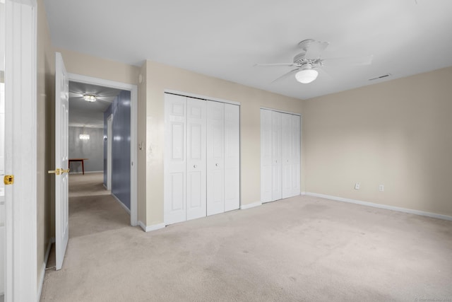 unfurnished bedroom with two closets, light colored carpet, visible vents, ceiling fan, and baseboards