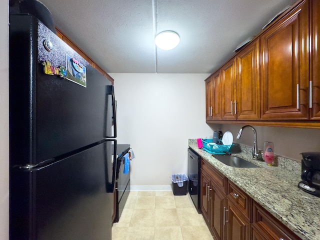 kitchen with light stone counters, brown cabinetry, a sink, black appliances, and baseboards