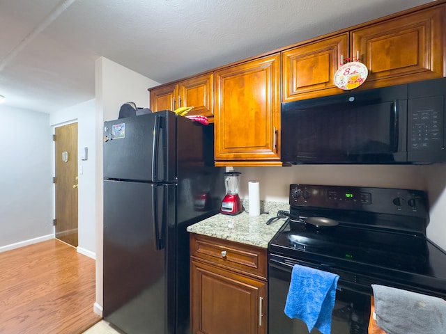 kitchen featuring light stone counters, baseboards, brown cabinets, black appliances, and light wood finished floors