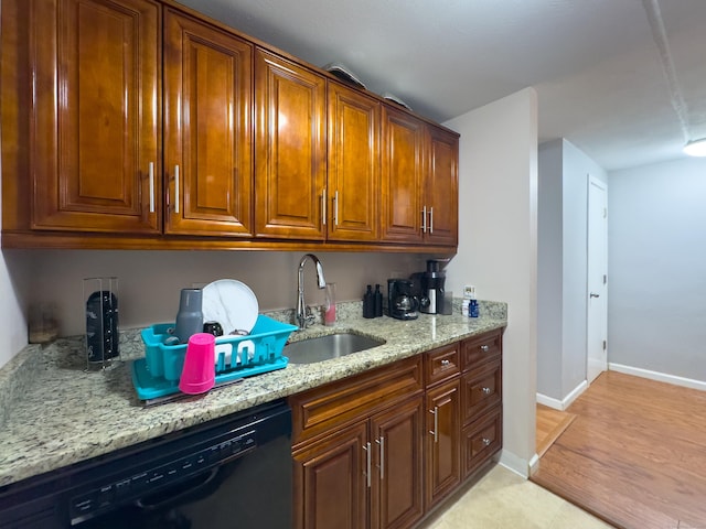 kitchen featuring light stone counters, black dishwasher, brown cabinets, a sink, and baseboards