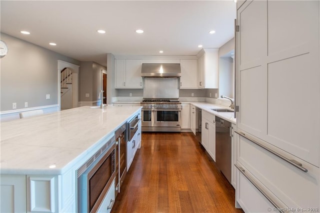 kitchen featuring light stone counters, a sink, white cabinetry, appliances with stainless steel finishes, and ventilation hood