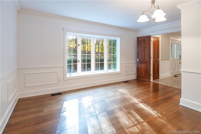 empty room with visible vents, wood finished floors, an inviting chandelier, crown molding, and a decorative wall