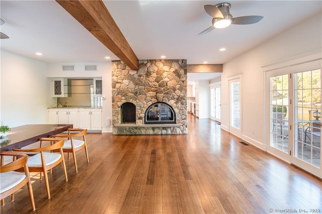 living room featuring a stone fireplace, a ceiling fan, visible vents, light wood-style floors, and beam ceiling