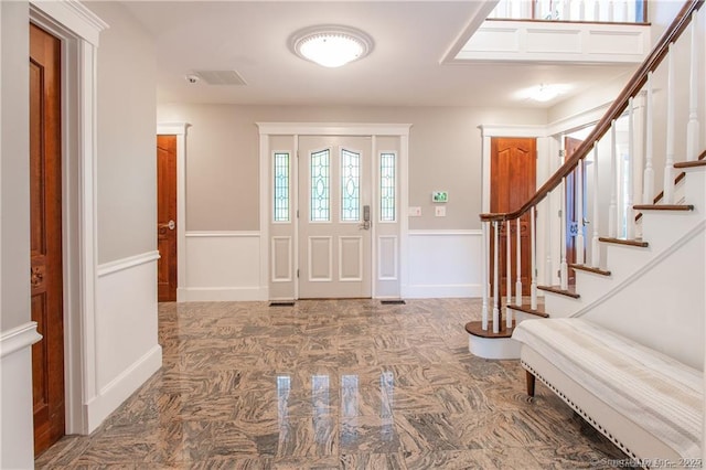 entrance foyer with a decorative wall, a wainscoted wall, visible vents, marble finish floor, and stairway