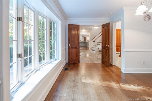 interior space featuring wood finished floors, visible vents, baseboards, stairs, and ornamental molding