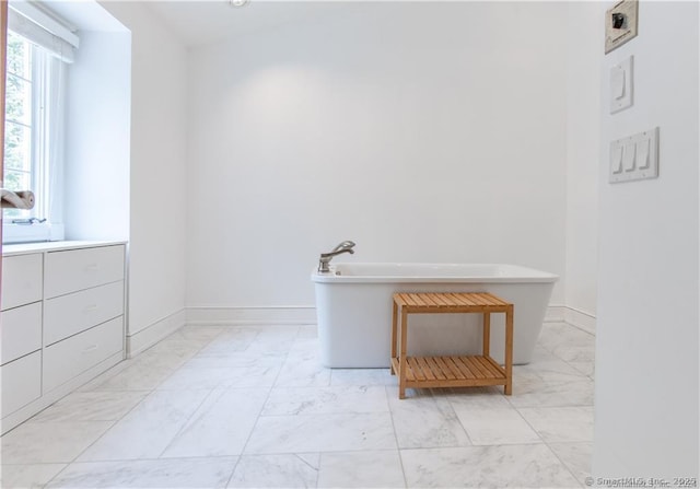 bathroom with marble finish floor, baseboards, and a freestanding tub