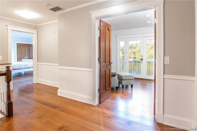 corridor featuring french doors, visible vents, ornamental molding, wood finished floors, and baseboards