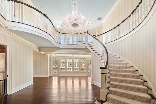 foyer entrance with a towering ceiling, visible vents, ornamental molding, an inviting chandelier, and wallpapered walls