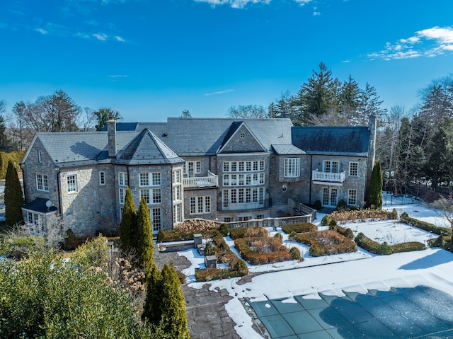 back of house with stone siding, a chimney, a patio area, and a balcony