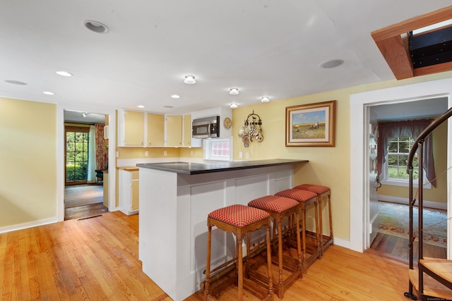 kitchen featuring stainless steel microwave, light wood-style floors, a healthy amount of sunlight, and a breakfast bar area