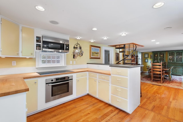 kitchen featuring light wood-type flooring, recessed lighting, stainless steel appliances, a peninsula, and wooden counters