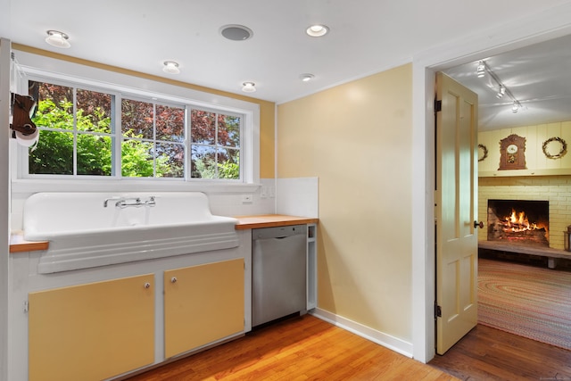 kitchen featuring a fireplace, a sink, light wood-style floors, dishwasher, and tasteful backsplash