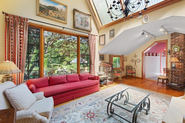 living area featuring vaulted ceiling, a notable chandelier, rail lighting, and wood finished floors