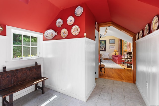 hallway with tile patterned floors, wainscoting, and vaulted ceiling