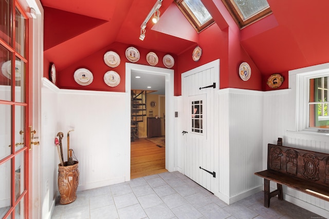 interior space featuring tile patterned floors, vaulted ceiling with skylight, rail lighting, and a wainscoted wall