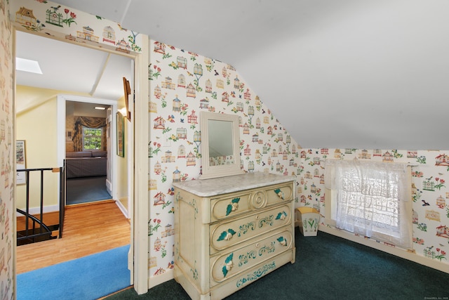 additional living space with baseboards, lofted ceiling with skylight, wood finished floors, and wallpapered walls