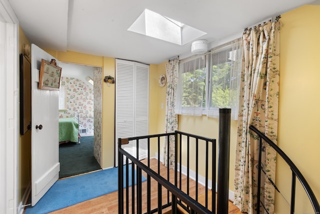 hallway featuring an upstairs landing, a skylight, and wood finished floors