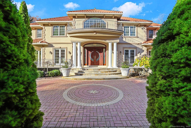 view of front of house featuring a balcony, curved driveway, a tiled roof, french doors, and stucco siding