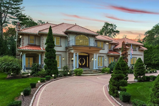 mediterranean / spanish home with decorative driveway, a chimney, stucco siding, a balcony, and a tiled roof