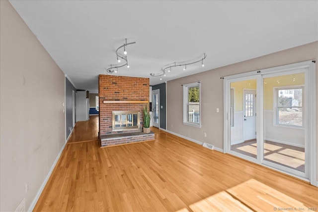 unfurnished living room with a brick fireplace, visible vents, baseboards, light wood-style floors, and track lighting