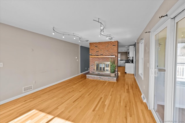 unfurnished living room featuring baseboards, visible vents, light wood-type flooring, a brick fireplace, and track lighting