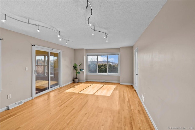 spare room with rail lighting, visible vents, a textured ceiling, wood finished floors, and baseboards