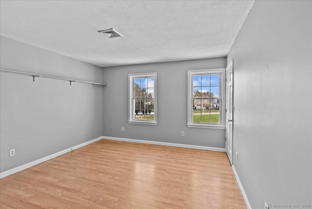 empty room featuring light wood-style floors, visible vents, a textured ceiling, and baseboards