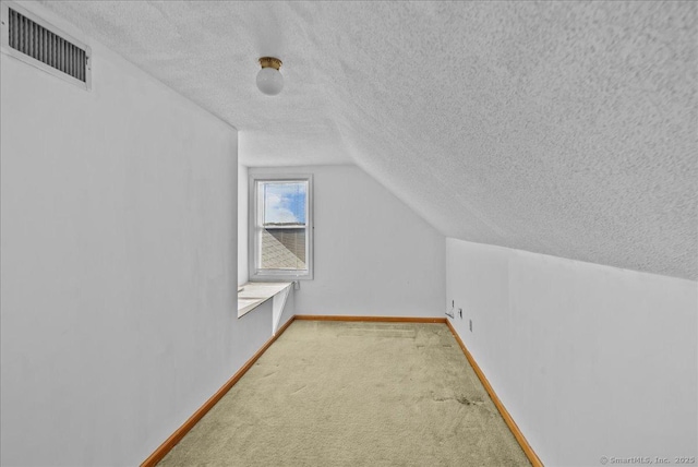 additional living space featuring a textured ceiling, visible vents, vaulted ceiling, and carpet flooring