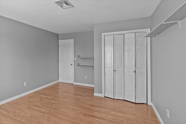 unfurnished bedroom with light wood-type flooring, visible vents, a textured ceiling, and baseboards