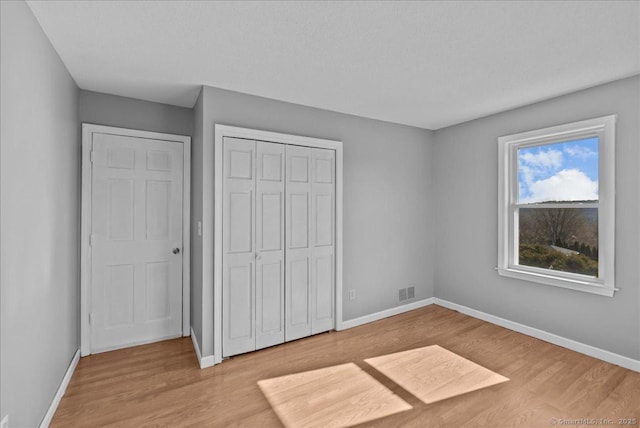 unfurnished bedroom featuring a closet, visible vents, baseboards, and wood finished floors