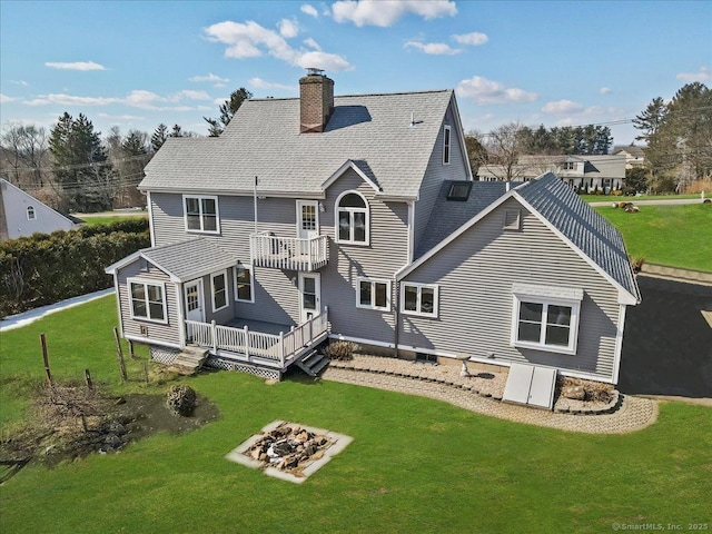 rear view of property with a yard, a chimney, a shingled roof, a fire pit, and a wooden deck