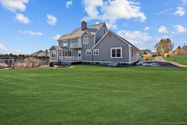 back of property with a balcony, a chimney, and a lawn