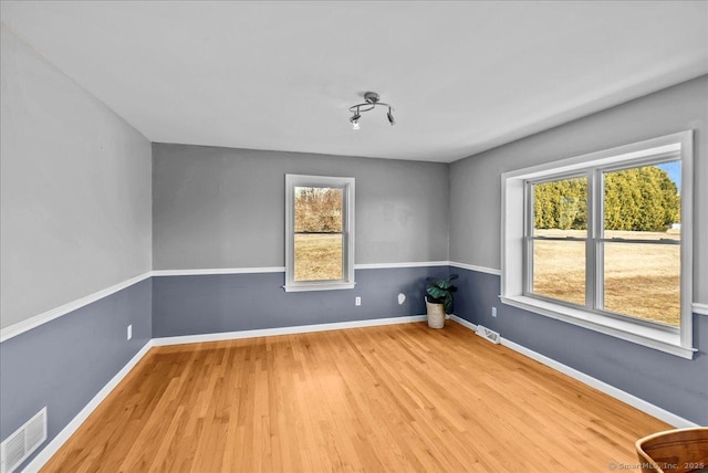 empty room with wood finished floors, visible vents, and baseboards