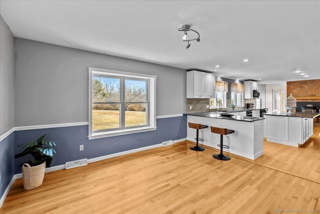 kitchen with decorative backsplash, dark countertops, a peninsula, light wood-type flooring, and white cabinetry