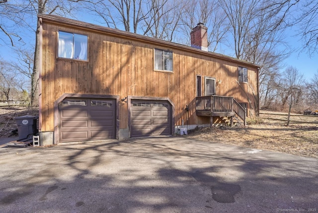 exterior space with aphalt driveway, a chimney, and a garage