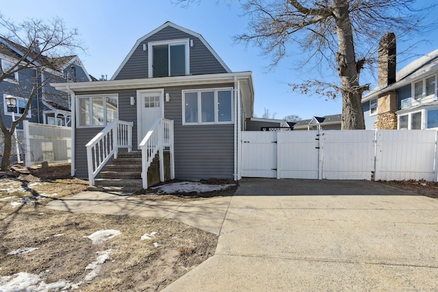 view of front facade with a gate, driveway, a gambrel roof, and fence