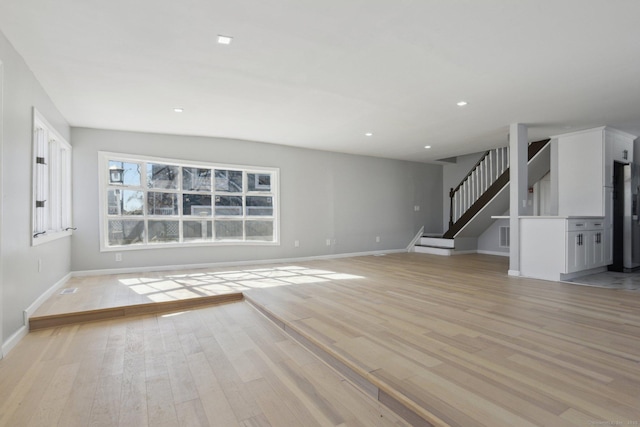 unfurnished living room featuring light wood-type flooring, recessed lighting, baseboards, and stairs