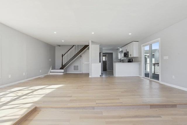 unfurnished living room with recessed lighting, visible vents, stairway, and light wood finished floors