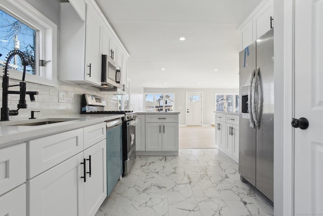 kitchen featuring a sink, white cabinets, marble finish floor, appliances with stainless steel finishes, and decorative backsplash