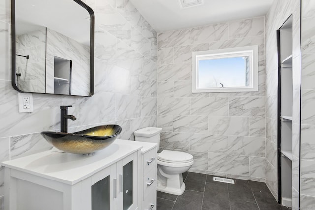 full bathroom with tile walls, visible vents, vanity, and toilet